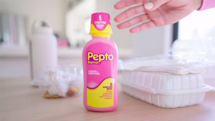 A bottle of Pepto Bismol 5-Symptom Relief liquid sitting on a kitchen counter with takeout containers.