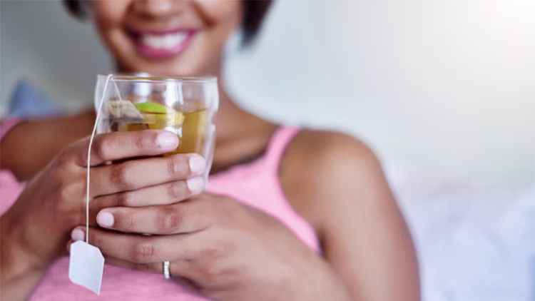 Close-up of a smiling woman holding a warm glass of herbal tea with a lemon slice.