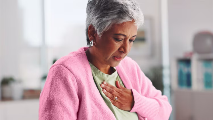 An older woman looking down with a concerned expression, holding her hand to her chest to indicate heartburn.