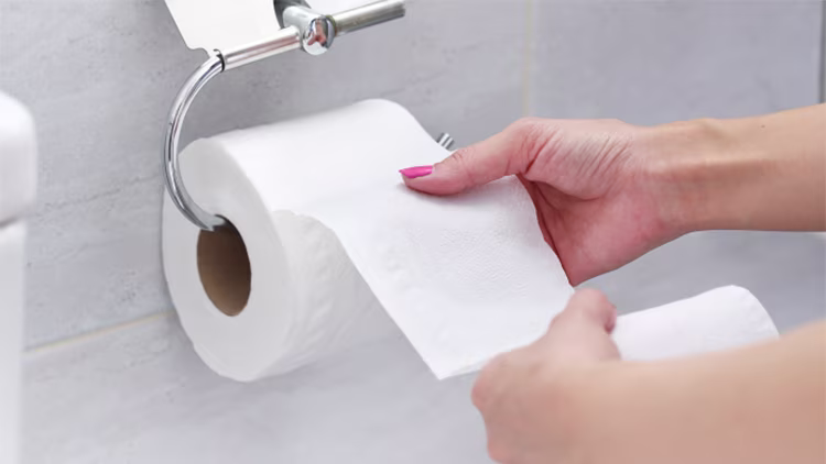 Close-up of a person's hands reaching for and pulling a sheet of toilet paper from a roll.