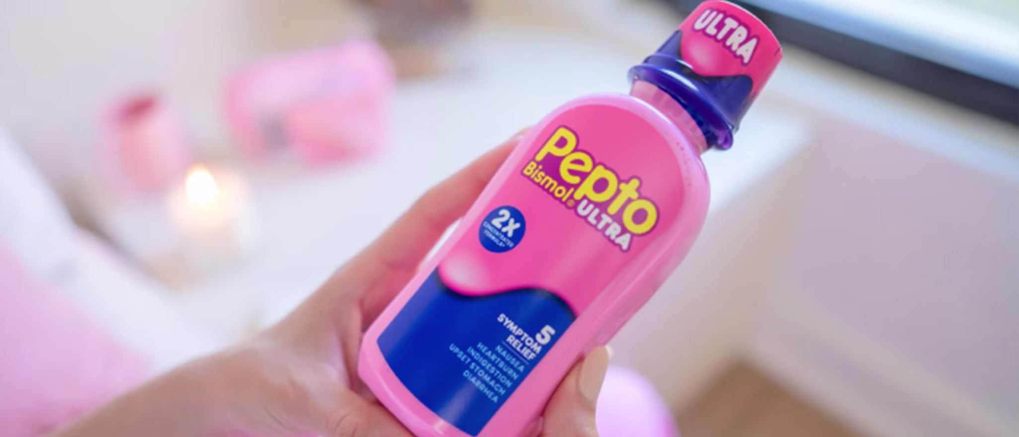 Close-up of hands holding a bottle of Pepto Bismol Ultra liquid in a bright, modern room.