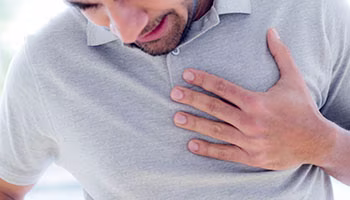 A man in pain placing his hand on the chest in gray t-shirt.