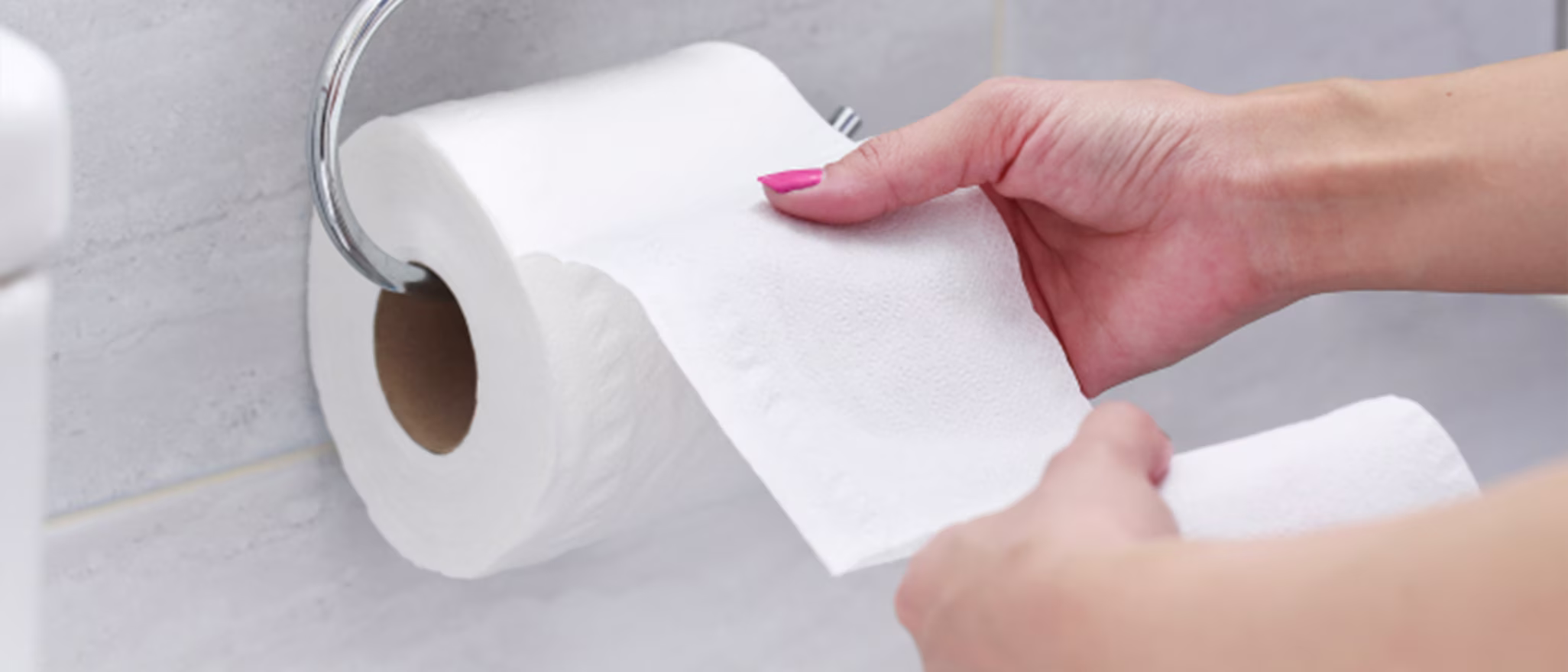 Close-up of a person's hands reaching for and pulling a sheet of toilet paper from a roll.