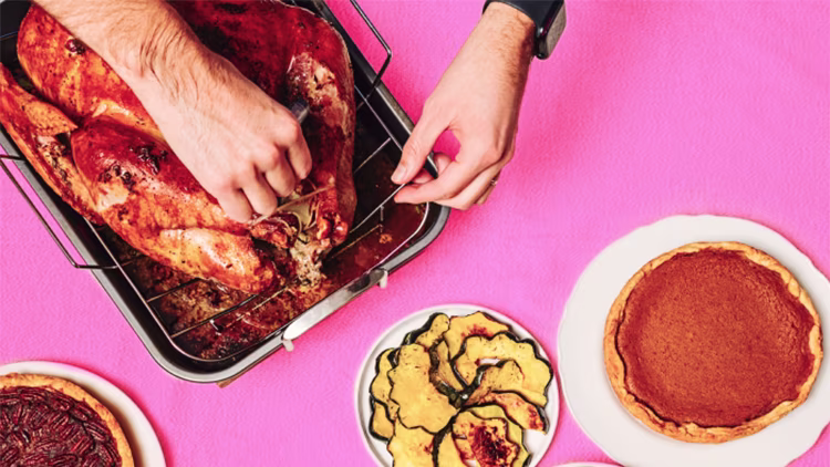 Top-down view of a person carving a roasted turkey on a table set with pies.