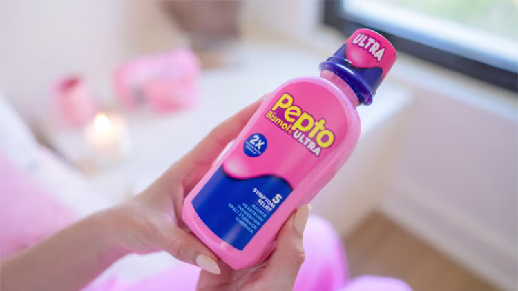Close-up of hands holding a bottle of Pepto Bismol Ultra liquid in a bright, modern room.