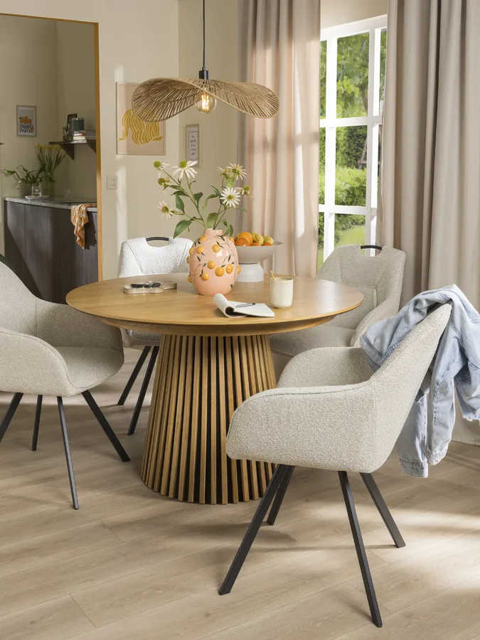 Moderne eetkamer met ronde houten tafel, beige stoelen en rotan hanglamp.