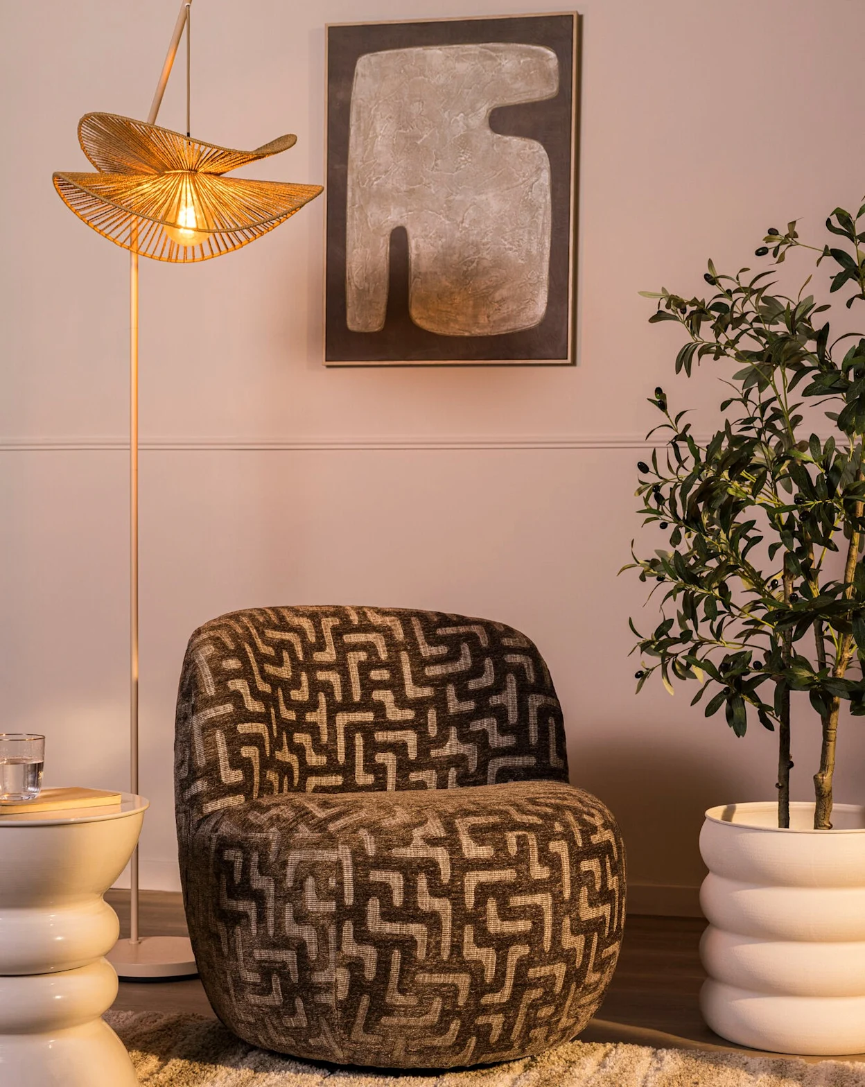 Fauteuil met grafisch patroon in een warm interieur met een vloerlamp, kunstwerk en groene plant.