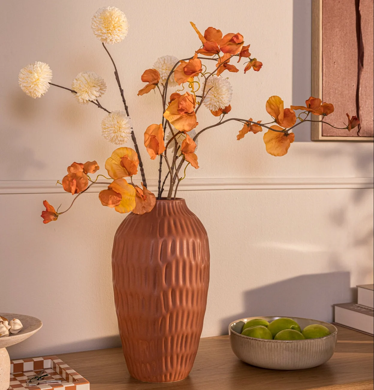 Bruine vaas met een reliëf en oranje takken op een houten dressoir.