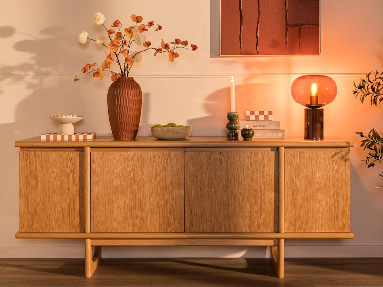 Houten dressoir met decoratie, vazen en sfeerverlichting in een warm interieur.