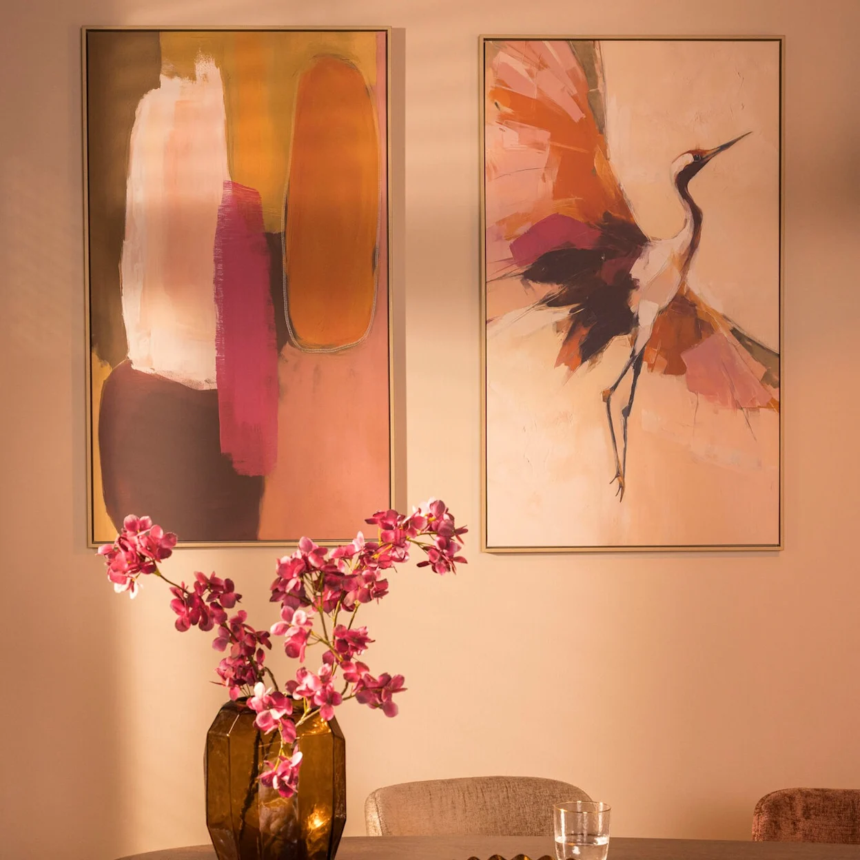 In roze tinten hangen twee schilderijen aan de wand: een abstract schilderij en een schilderij van een kraanvogel.