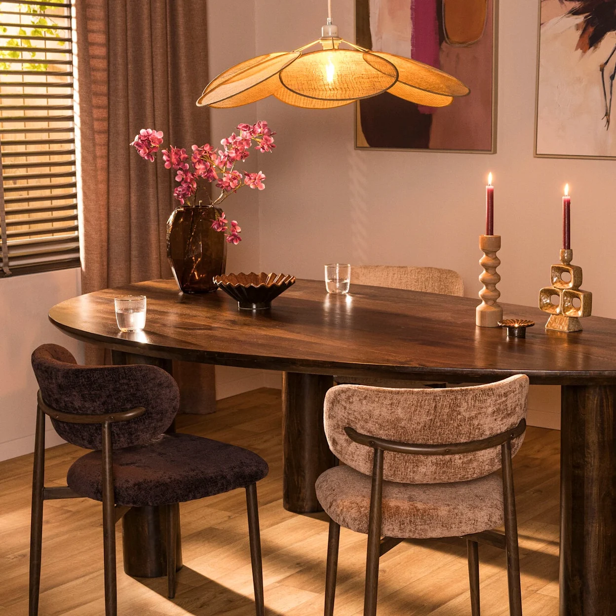 Warme eetkamer met houten eettafel, stoelen in twee kleuren en een bloemvormige hanglamp.