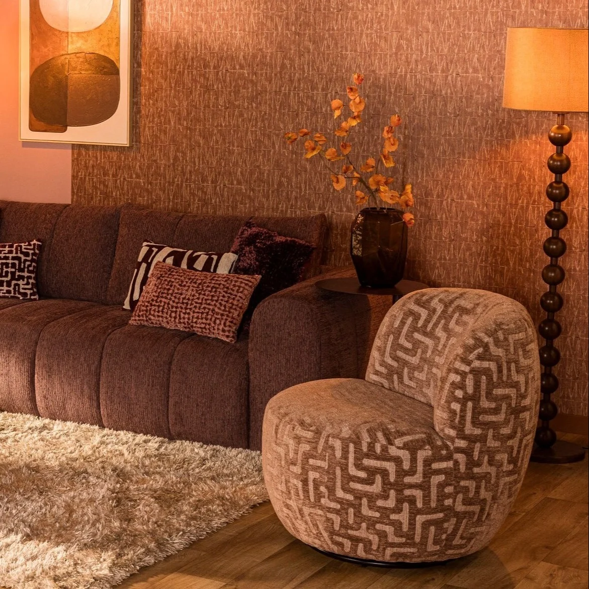 Woonkamer met een mauvekleurige bank en blush draaifauteuil met grafisch patroon in een warm interieur.