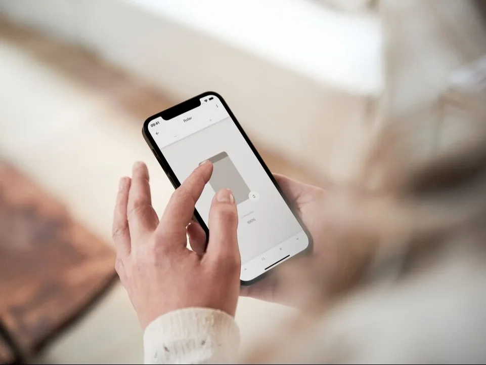 Vrouw houdt telefoon vast en bedient haar raambekleding via de app