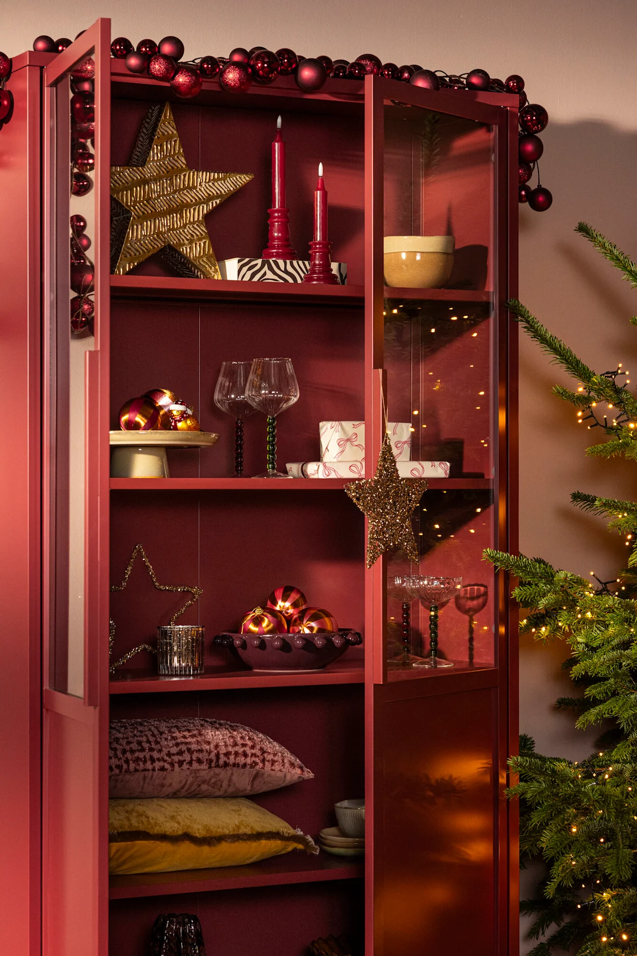 Bordeauxrode vitrinekast met kerstdecoratie en gouden kerstornamenten.