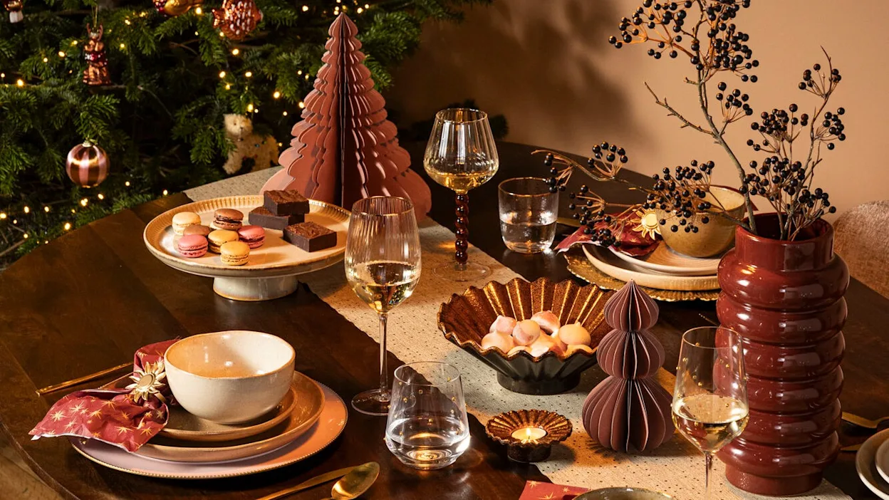 Feestelijk gedekte kersttafel met bordeaux, rood en gouden kerstdecoratie.