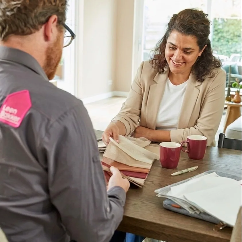 Een Leen Bakker adviseur zit aan tafel bij een vrouwelijke klant en toont haar verschillende staaltjes voor gordijnen