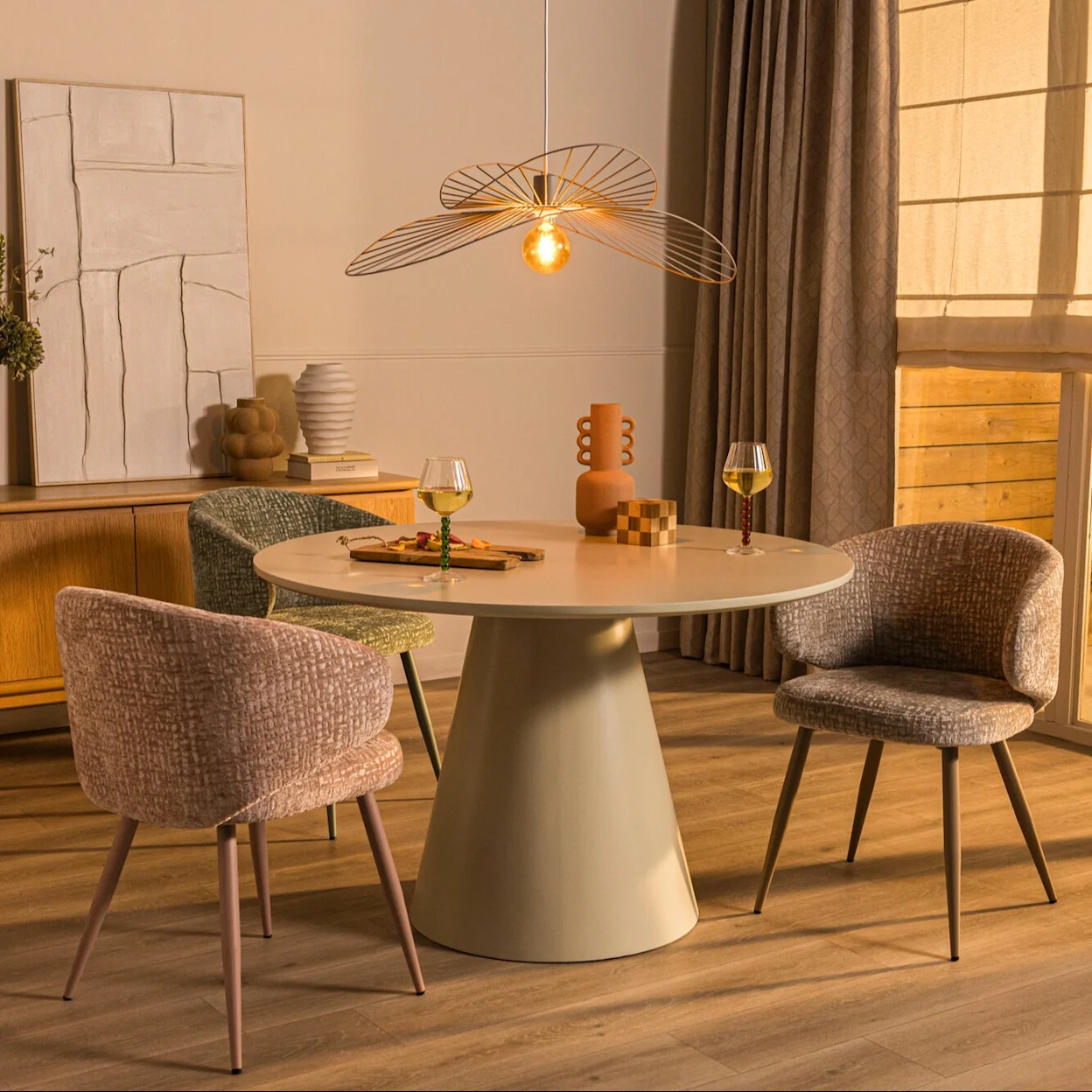 Natuurlijke eetkamer met een ronde eettafel, vier gestoffeerde eetkamerstoelen, houten dressoir en decoratieve verlichting.