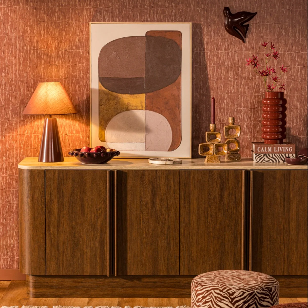 Houten dressoir met een tafellamp, schilderij en verschillende woonaccessoires.
