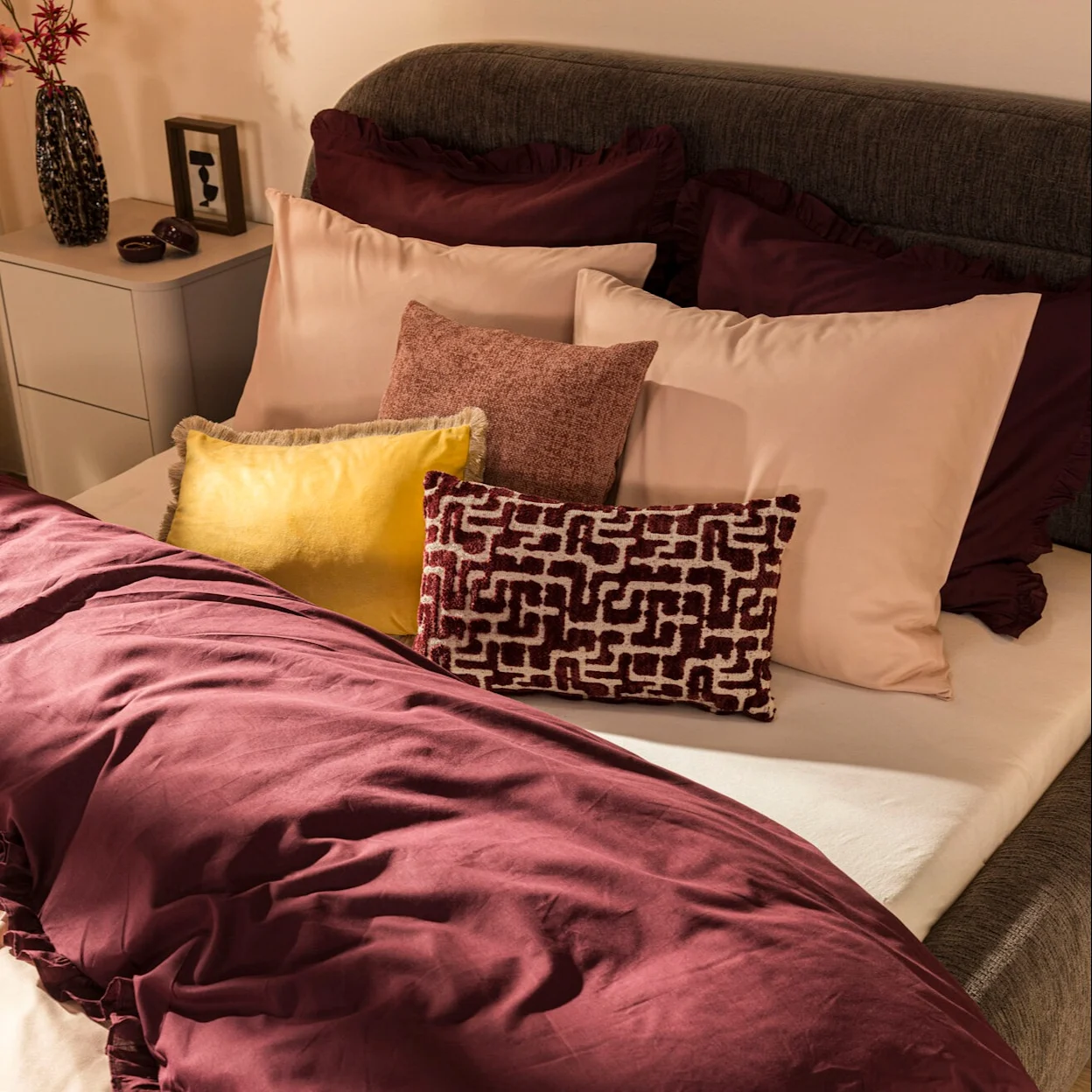 Ingezoomde foto van een bed met bordeaux dekbedovertrek en verschillende sierkussens.