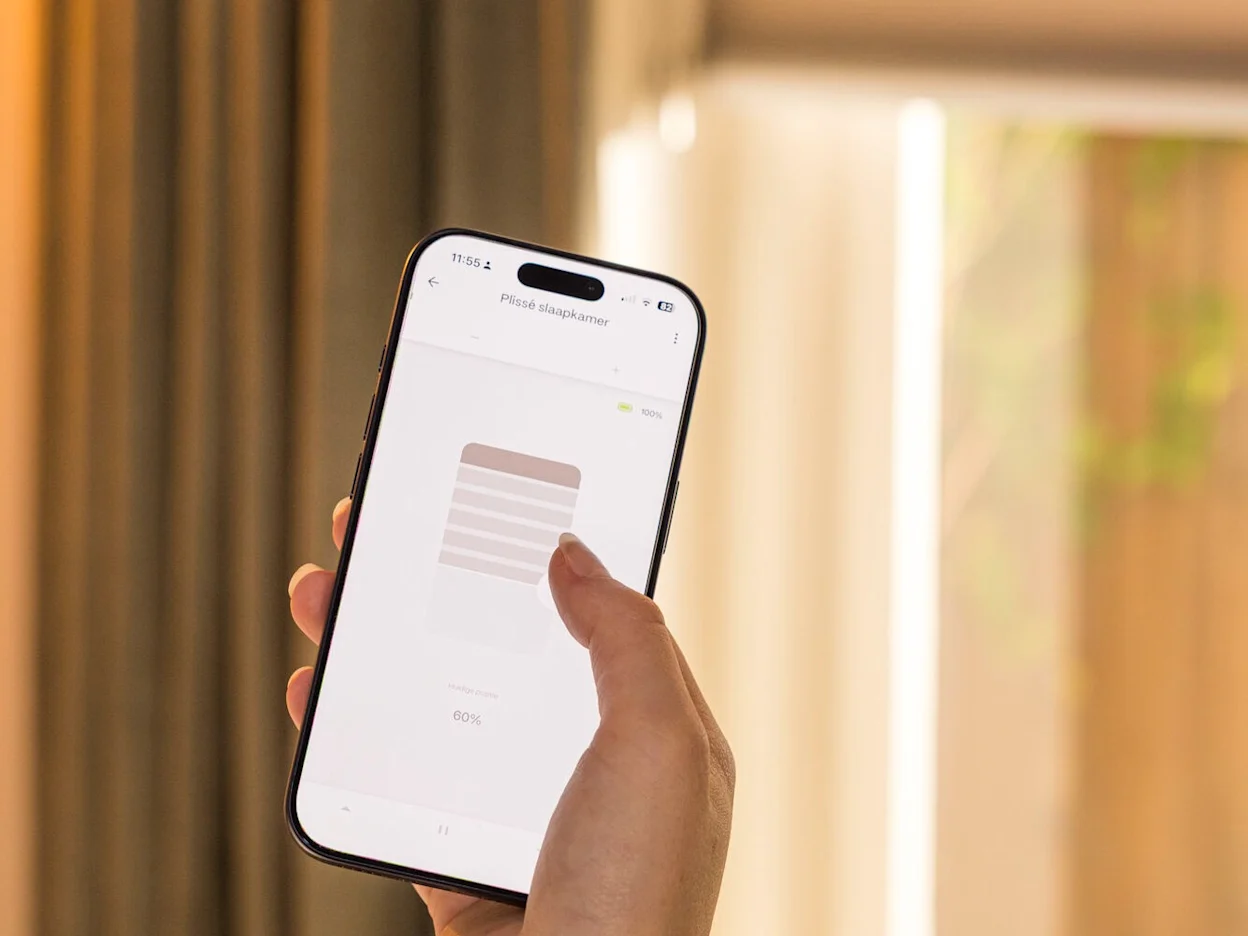 Een telefoon in de hand met een app voor de bediening van elektrische plisségordijnen
