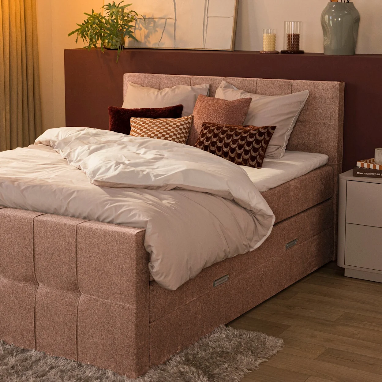 Lichtroze boxspring met gecapitonneerd hoofdbord en voetbord en een roze dekbedovertrek in een slaapkamer