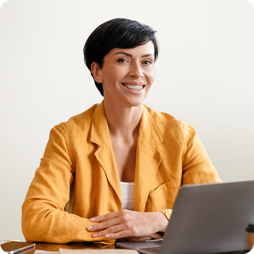 woman in yellow blazer smiling in front of a laptop