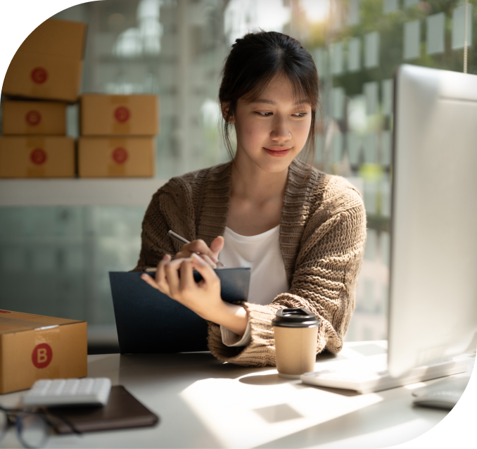 Image of a woman looking at pc while writing on a pad