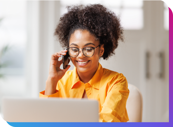 Woman sitting in front of laptop also talking on a mobile phone. 