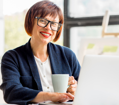 A Happy women working on her laptop with a coffee mug in one hand