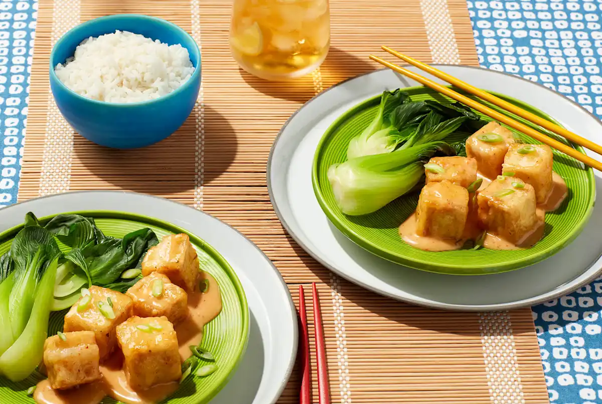 Fried tofu and bok choy on green plates, rice in a blue bowl with a bamboo background