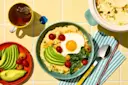 Breakfast with avocado, egg, hummus, and tea on a yellow tiled table.