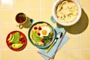 Breakfast with avocado, egg, hummus, and tea on a yellow tiled table.