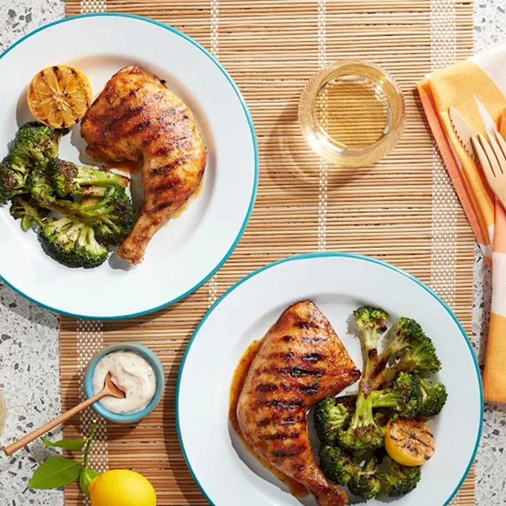 Grilled shrimp skewers with lemon wedges and green sauce on a platter, served with salad and dipping sauce on a blue plate.