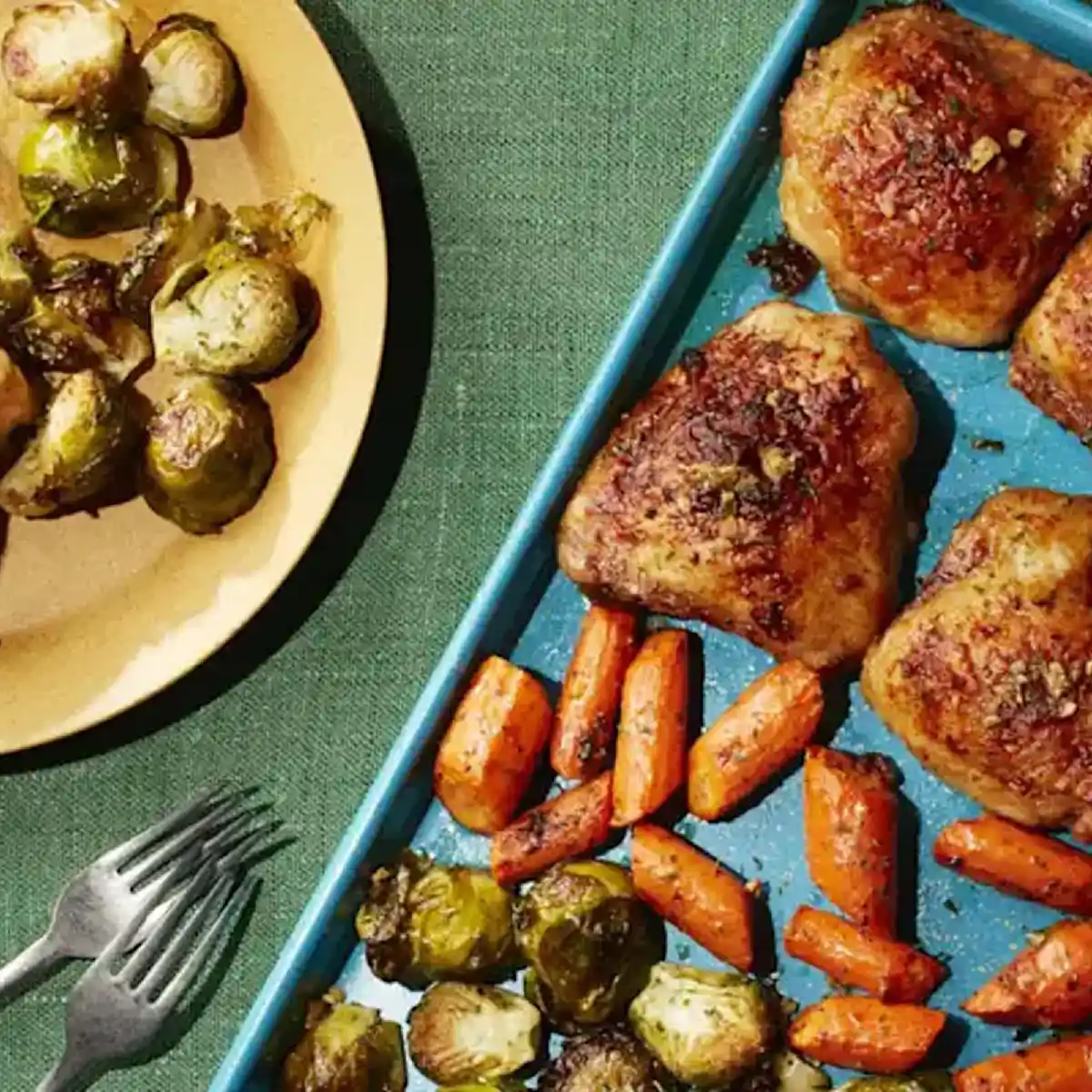 Baking sheet with roasted chicken, carrots and Brussels sprouts, next to a plate with sprouts on it