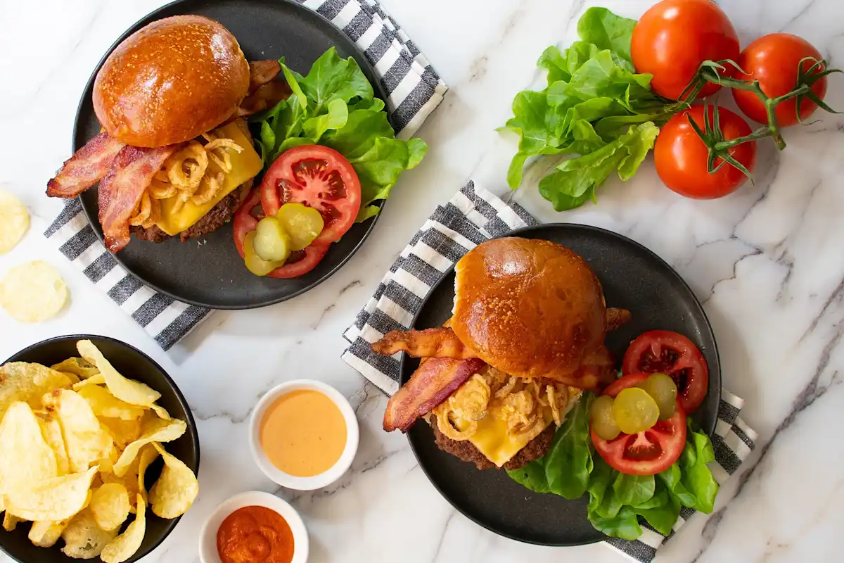 Black plateswith burgers and potato chips on striped napkins and marble counter