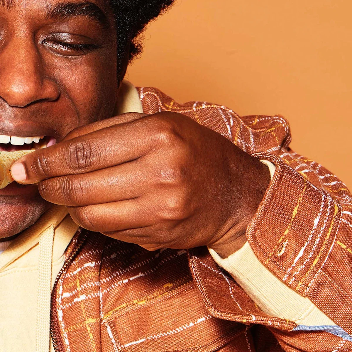 A man in a brown jacket eating a snack chip