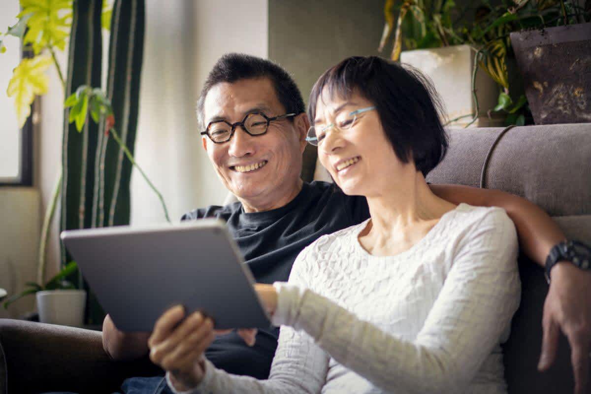 Older Asian couple smile while staring at a tablet together having found health insurance that covers pre-existing conditions