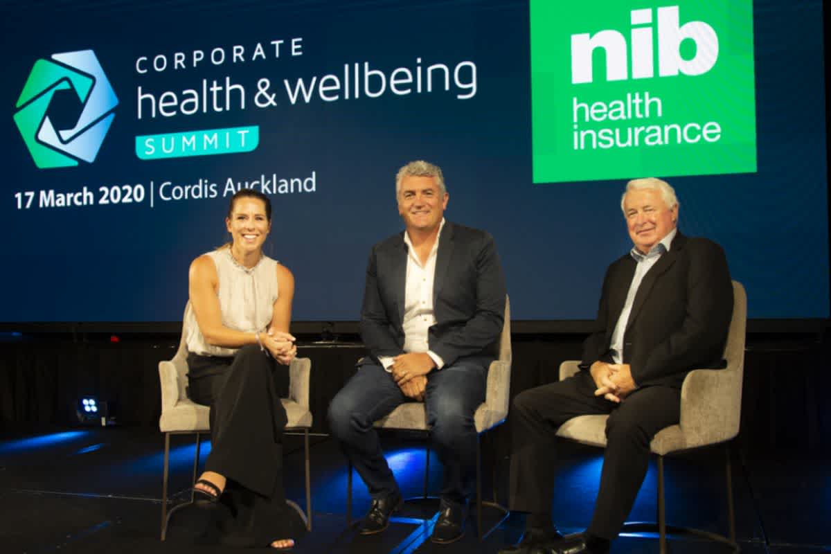 Two males and female sit on a stage at a panel about health and wellbeing at work