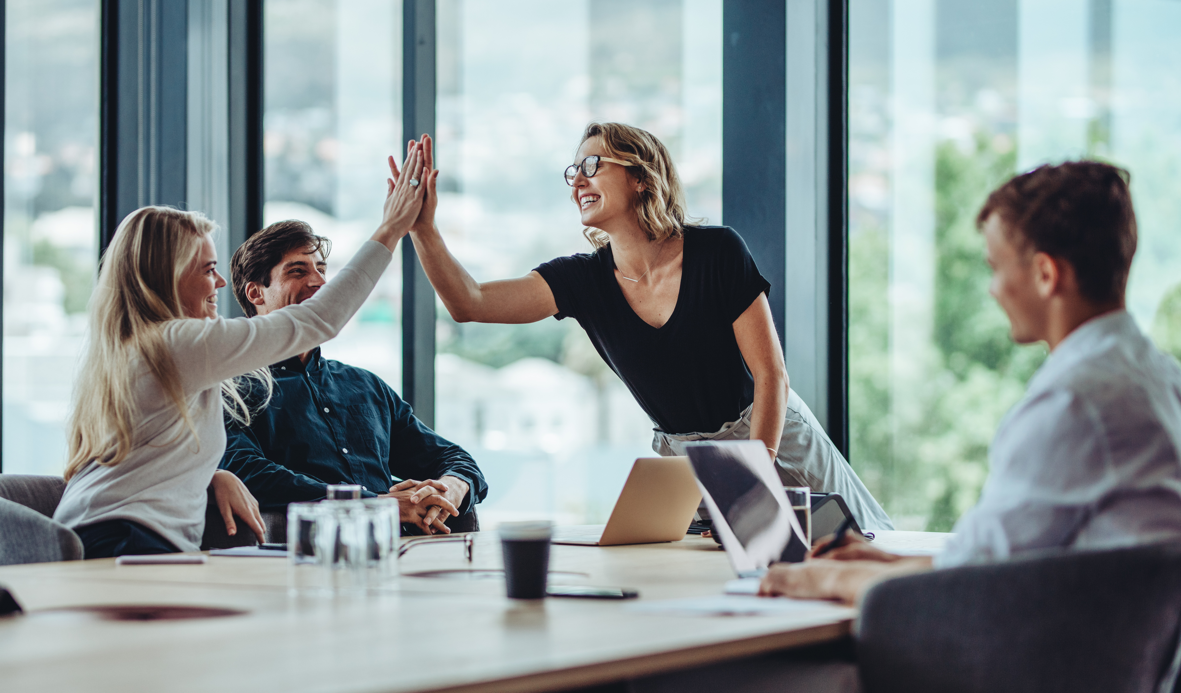 Colleagues high-fiving in a board room, showcasing workplace wellbeing