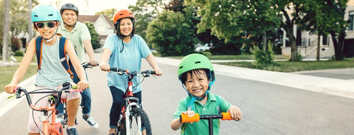 Family of four riding on a bicycle with their youngest smiling riding a scooter one of the many milestones from baby to toddlers