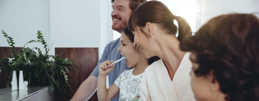 Parents laughing while brushing their teeth with kids knowing the price of a dentist check up cost in NZ