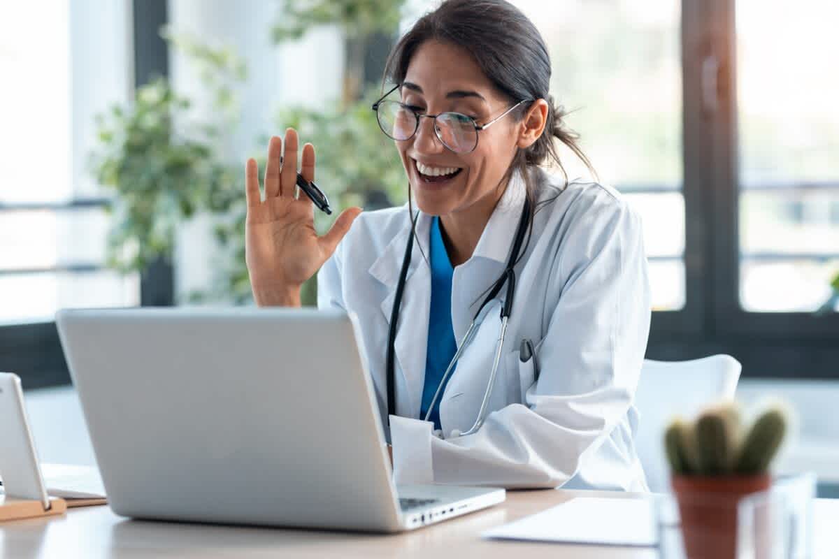 A female doctor waving at her laptop at a patient who decided to get a sick note online