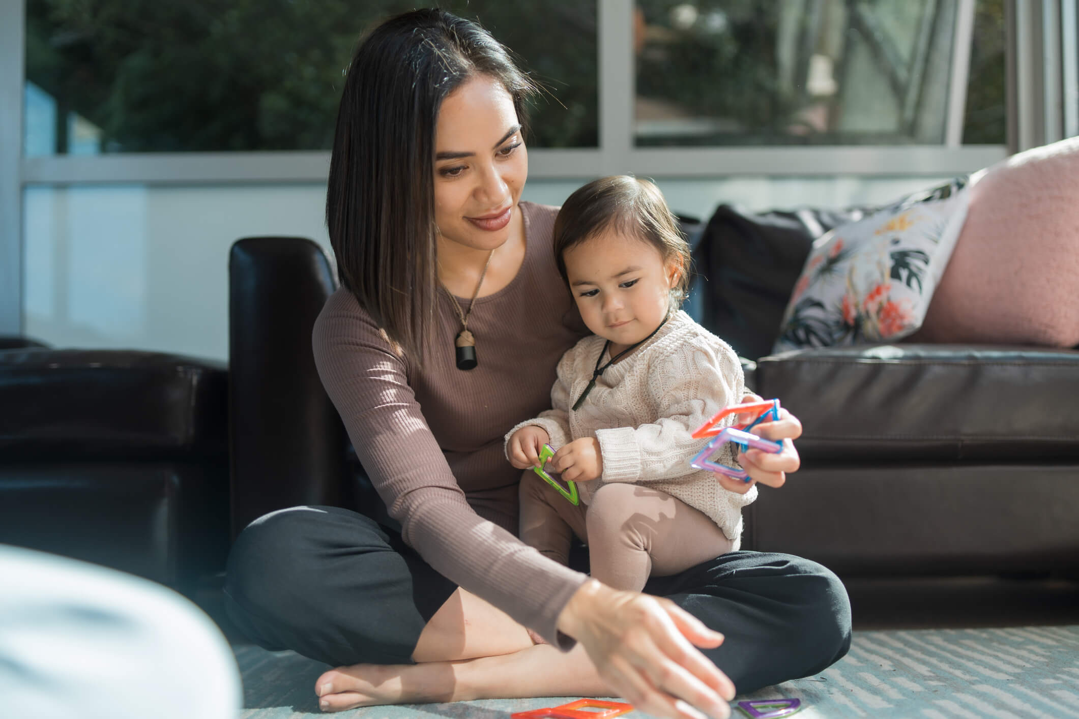 A young mother sits cross-legged with her daughter while thinking about her parental concern for her child's future mental health