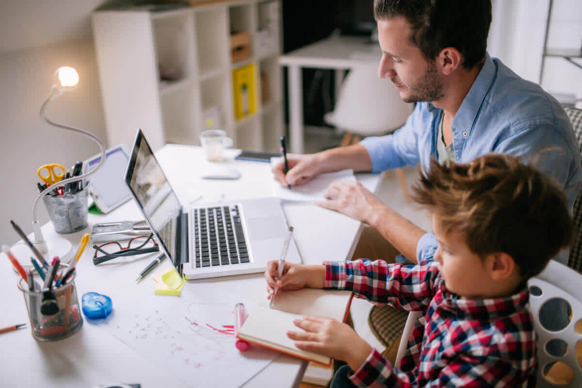 Father and son sitting at the same desk demonstrating that it is possible to be working from home with kids