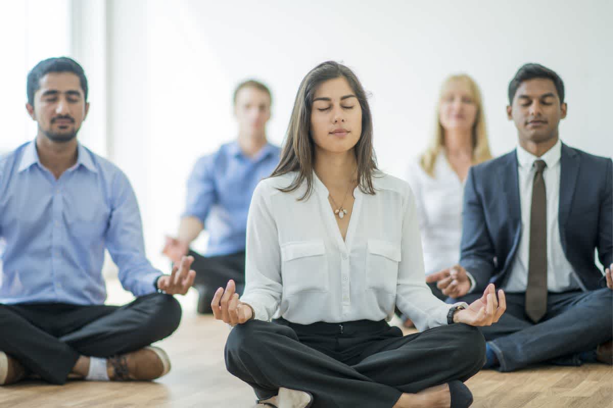 Five colleagues practise meditation in their office to improve mental wellbeing