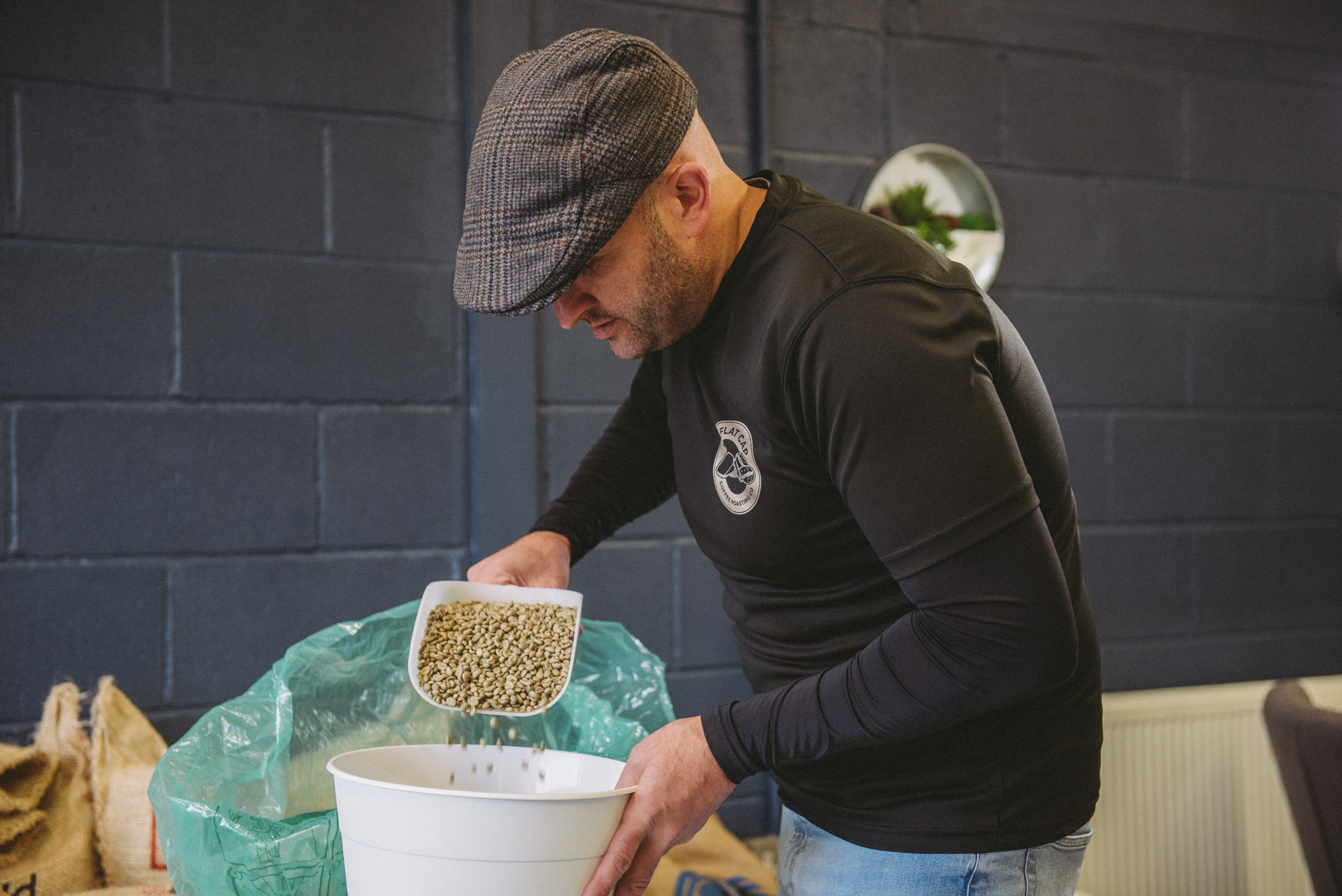 Mark of Flat Cap Coffee pouring unroasted coffee beans into a white bucket