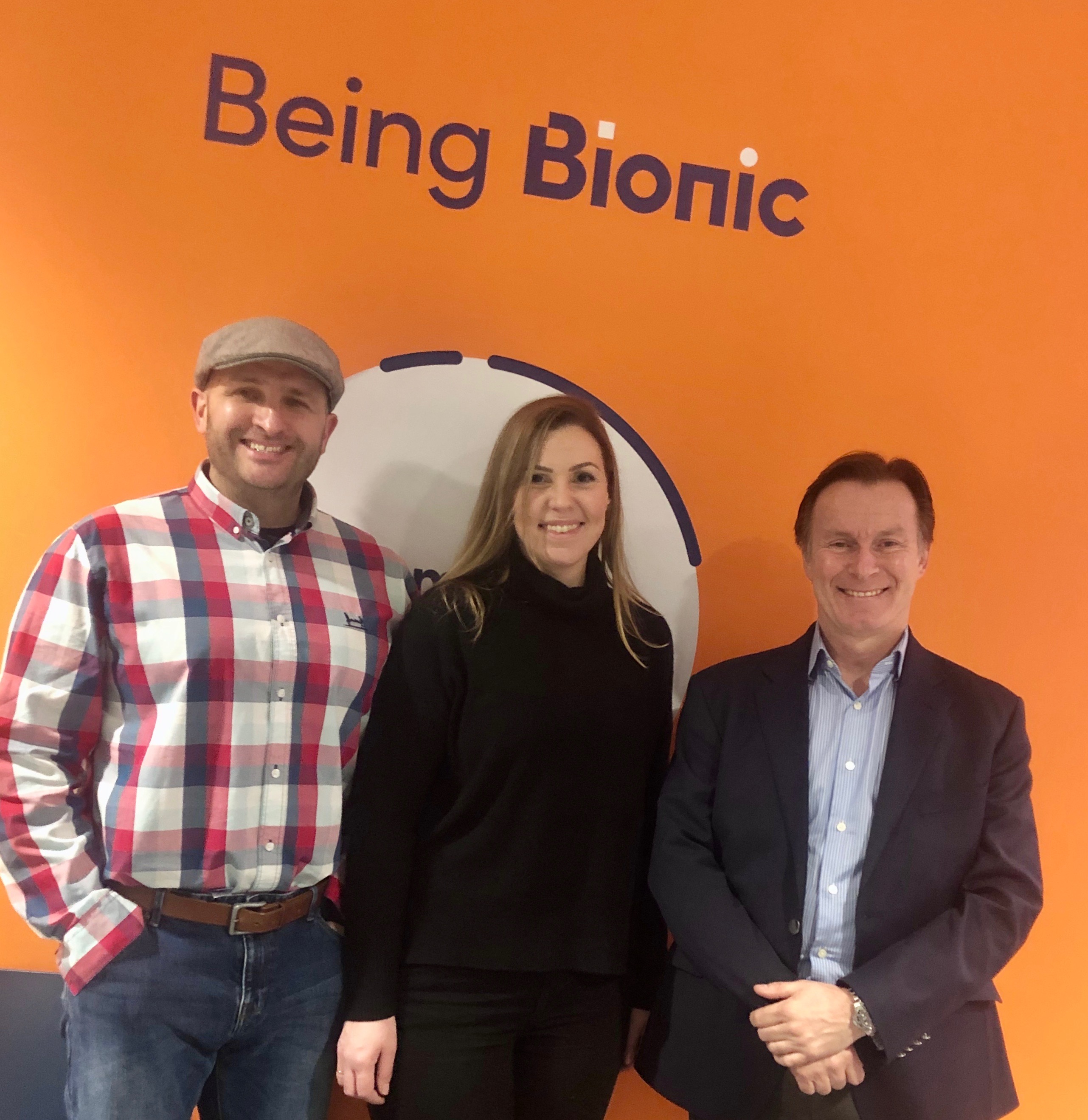 The Flat Cap team stood in front of an orange wall with Being Bionic written above them at Bionic HQ