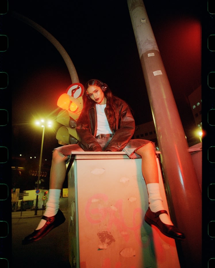 Woman sitting at night with a streetlight in the background, wearing Marshall Major V Black on-ear headphones.