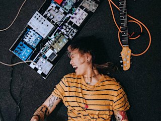 Yvette laying on the floor smiling next to her guitar and pedal board