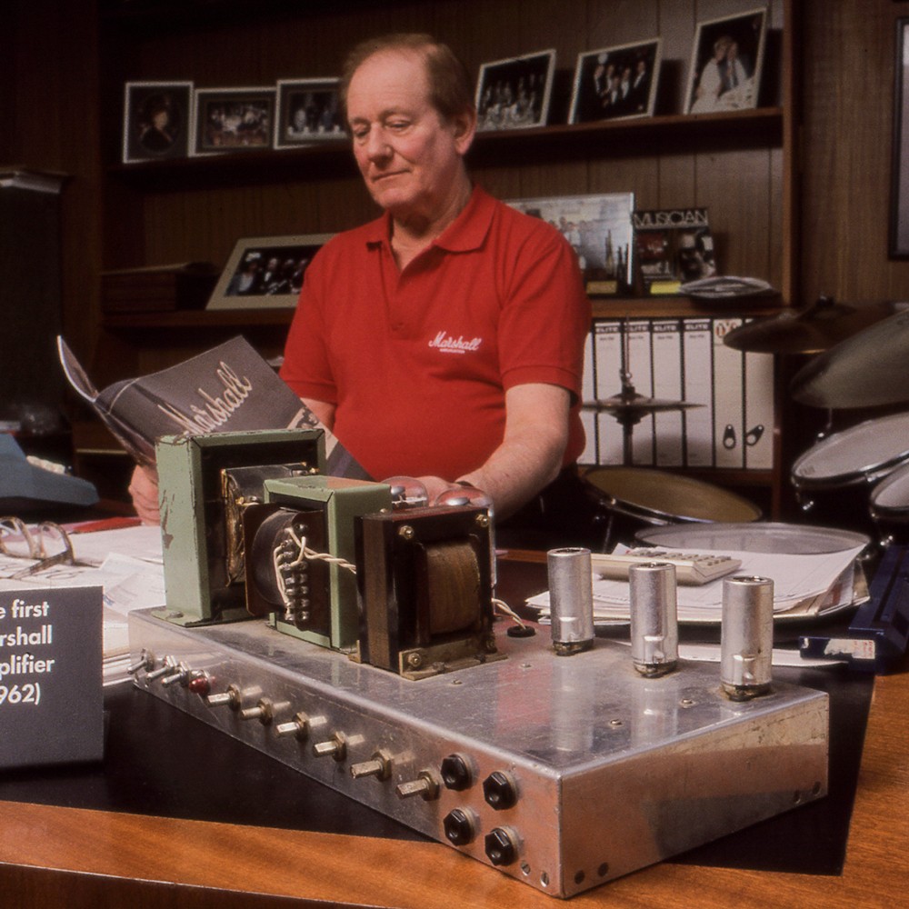 Image of Jim Marshall reading a Marshall paper in front of the first Marshall amplifier